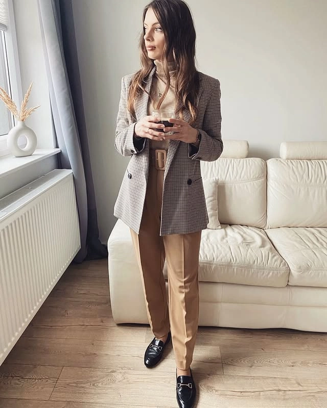 Woman standing in a bright living room wearing a beige turtleneck