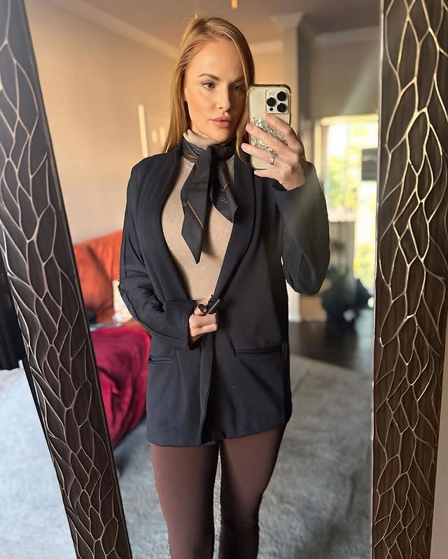 Woman wearing a beige turtleneck paired with a black blazer, a black scarf, and brown trousers