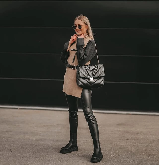 Woman wearing a beige turtleneck sweater vest layered over a black shirt.