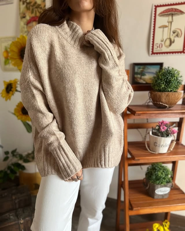 Woman wearing an oversized beige turtleneck sweater and white pants